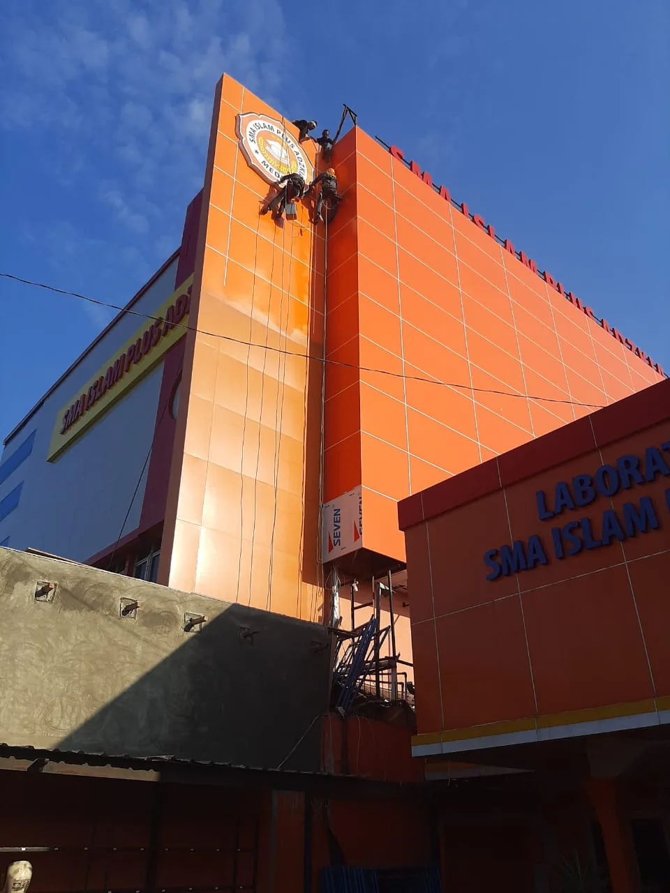 Pemasangan fasad ACP oranye pada bangunan sekolah